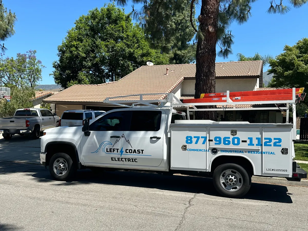Left Coast Electric service truck parked at the curb in front of a single-story home with a tile roof and a tall pine tree