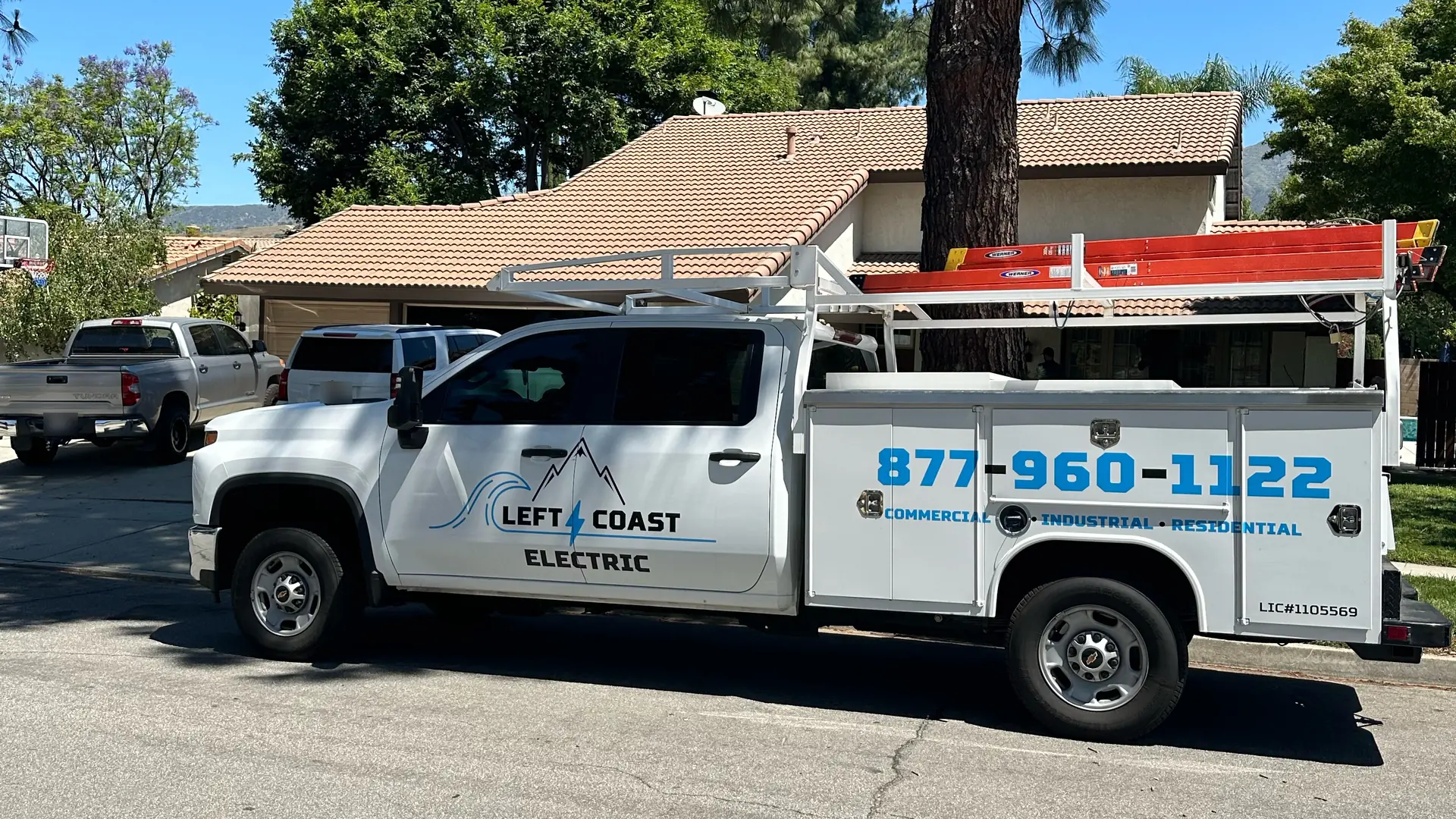 Left Coast Electric service truck parked at the curb in front of a single-story home with a tile roof and a tall pine tree