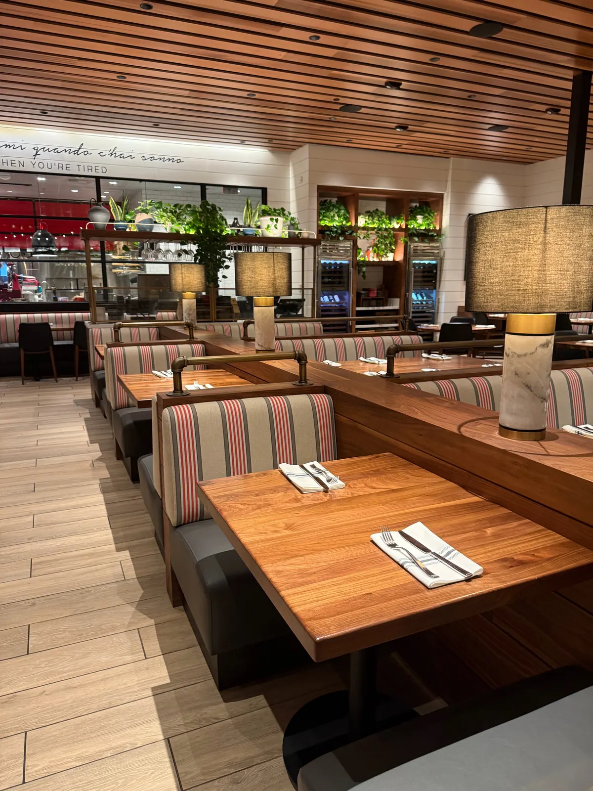 Striped booths with marble-base table lamps at North Italia in Brea, CA, with the open kitchen and wine refrigerators behind