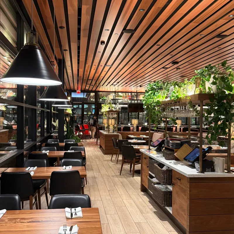 North Italia Brea dining room with black pendant lights over wood tables and recessed lights in a wood-slat ceiling