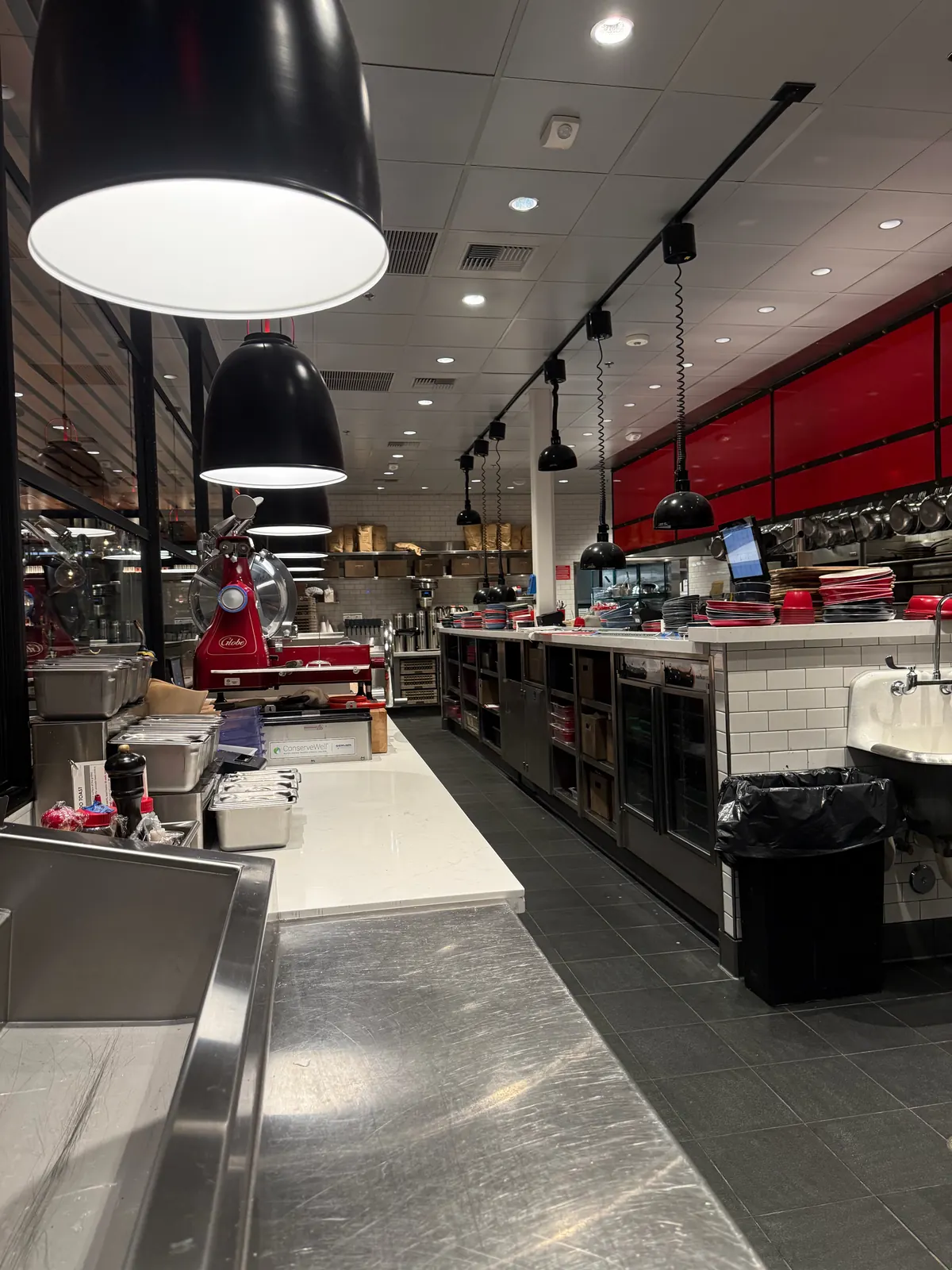Commercial kitchen line at North Italia Brea with black pendant lights, track lighting and recessed ceiling lights