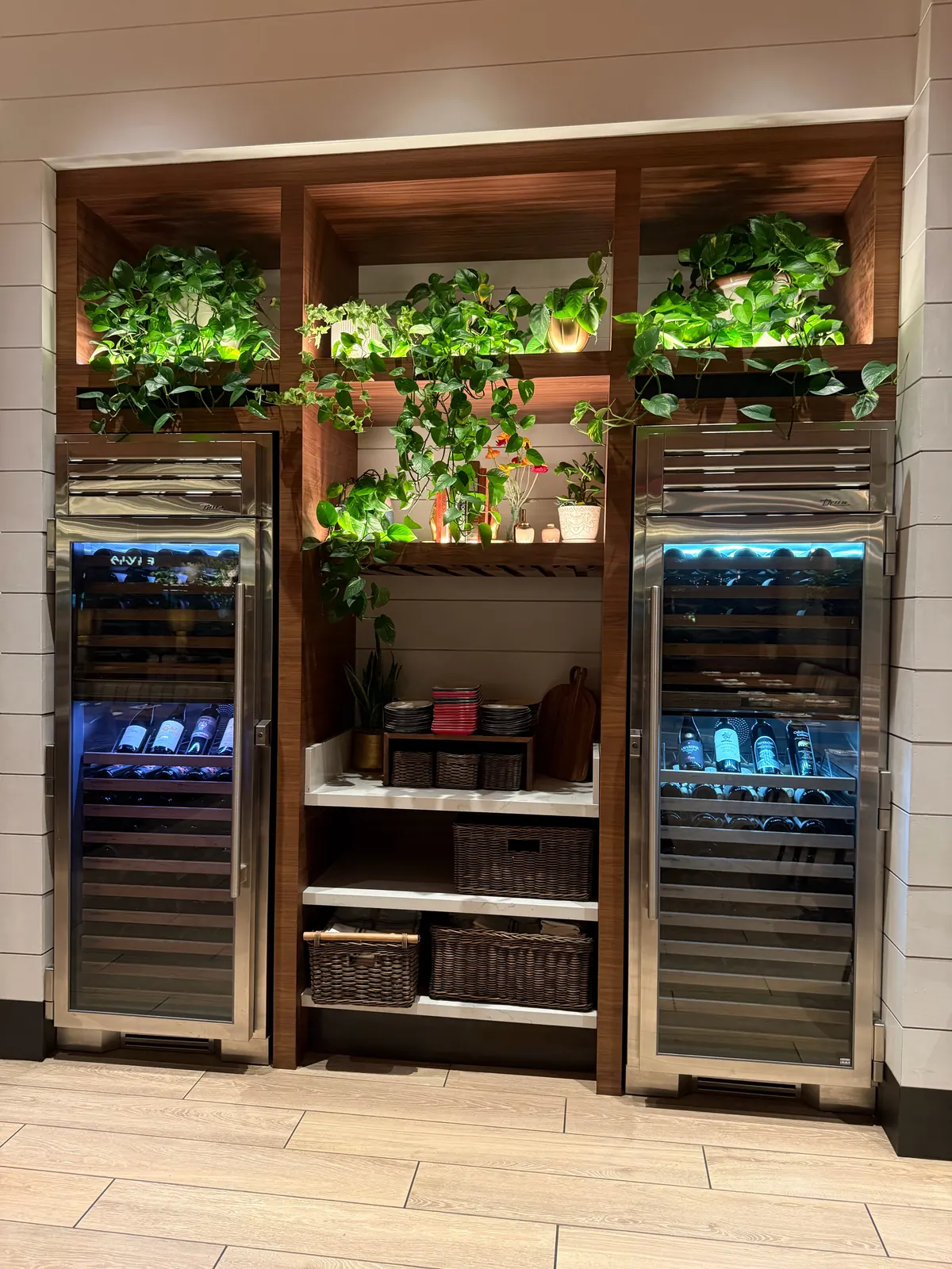 Two lit stainless-steel wine refrigerators on either side of wood shelving with plants at North Italia Brea