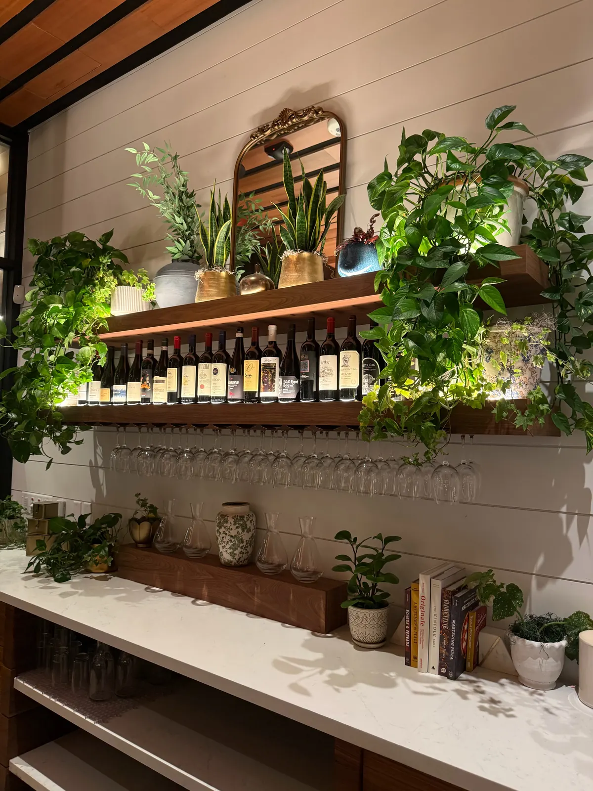 Wine bottles on a wood shelf with under-shelf LED lighting above hanging wine glasses at North Italia in Brea, CA
