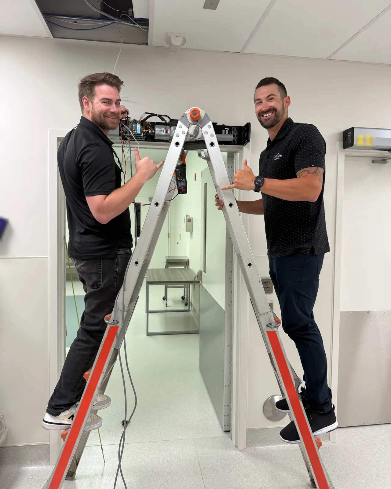 Two Left Coast Electric team members on a ladder at a doorway header with an open access-control panel at Ortho AZ in Glendale, AZ