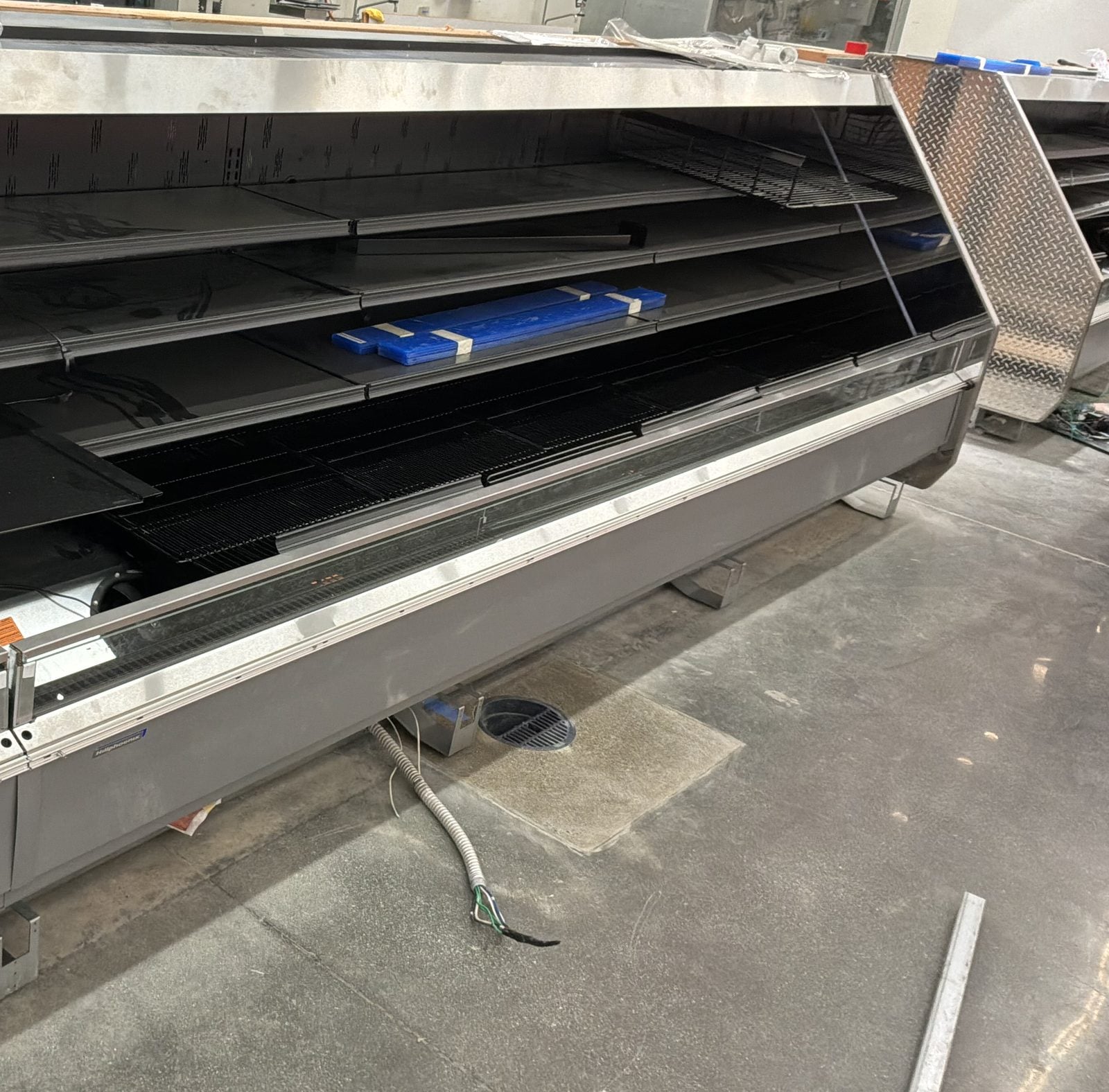Refrigerated display case at WinCo Foods in Hemet, CA with flexible conduit and wires stubbed out of the floor beside it