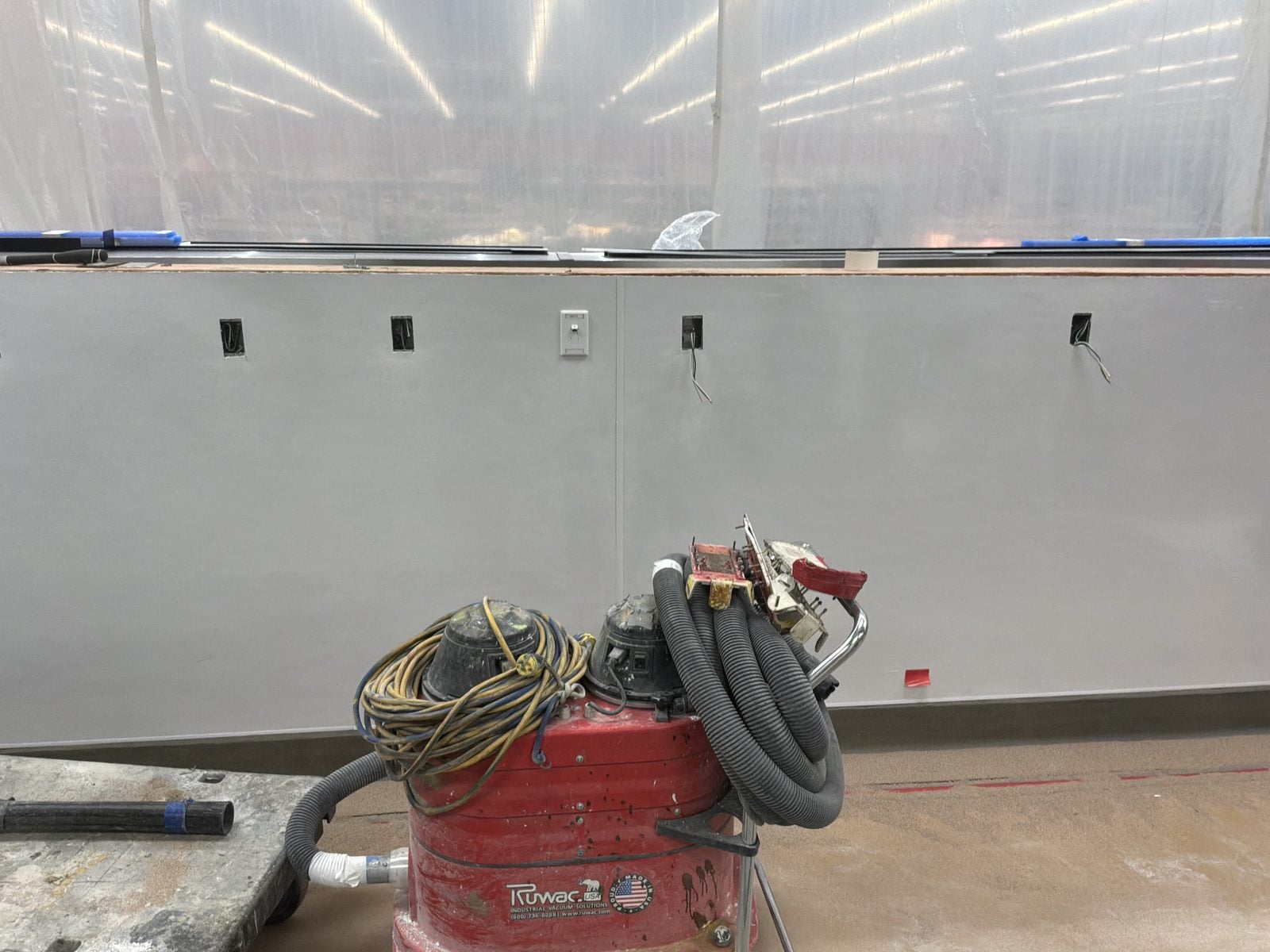 Finished gray wall with a row of receptacles and a shop vac on the floor at WinCo Foods in Hemet, CA