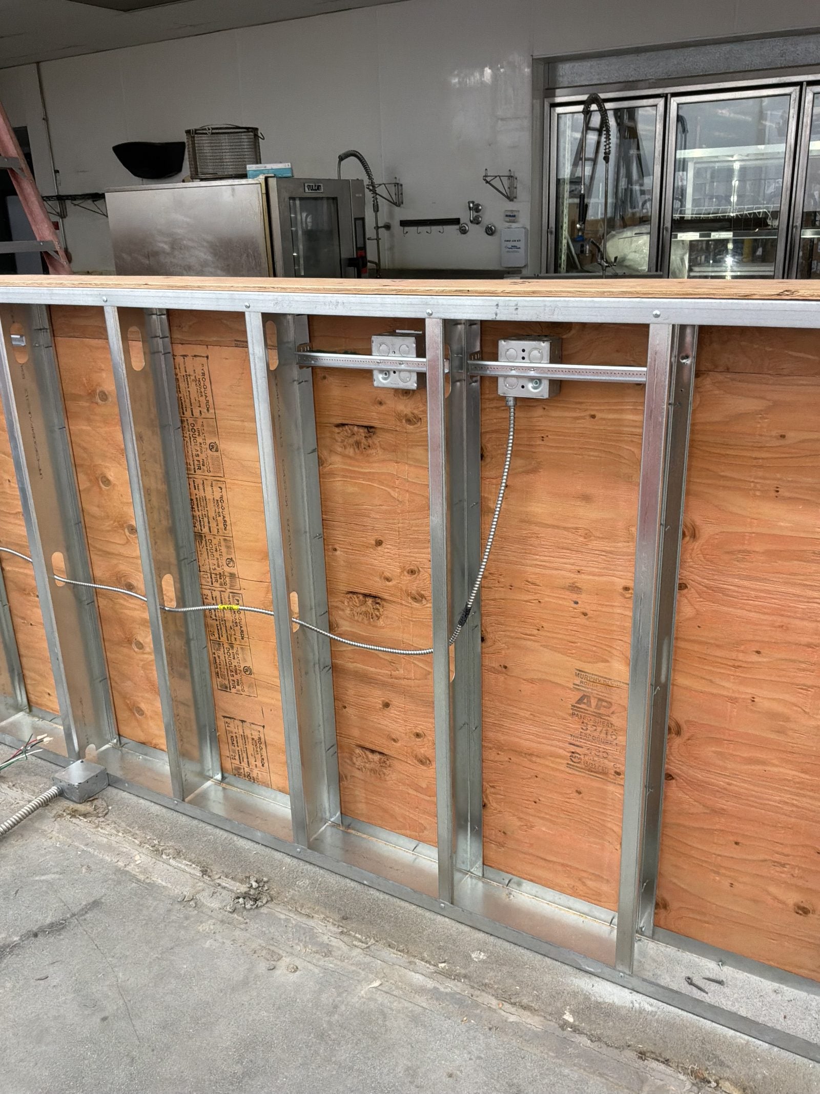 Framed wall with wood backing, metal outlet boxes and wiring runs for refrigerated cases at WinCo Foods in Hemet, CA