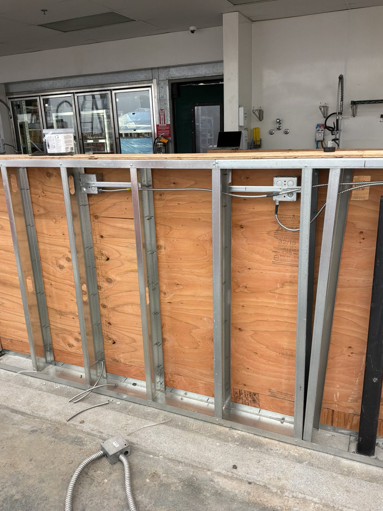 Framed wall with metal studs and wood backing, with conduit, wiring and outlet boxes roughed in at a WinCo Foods remodel in Hemet, CA