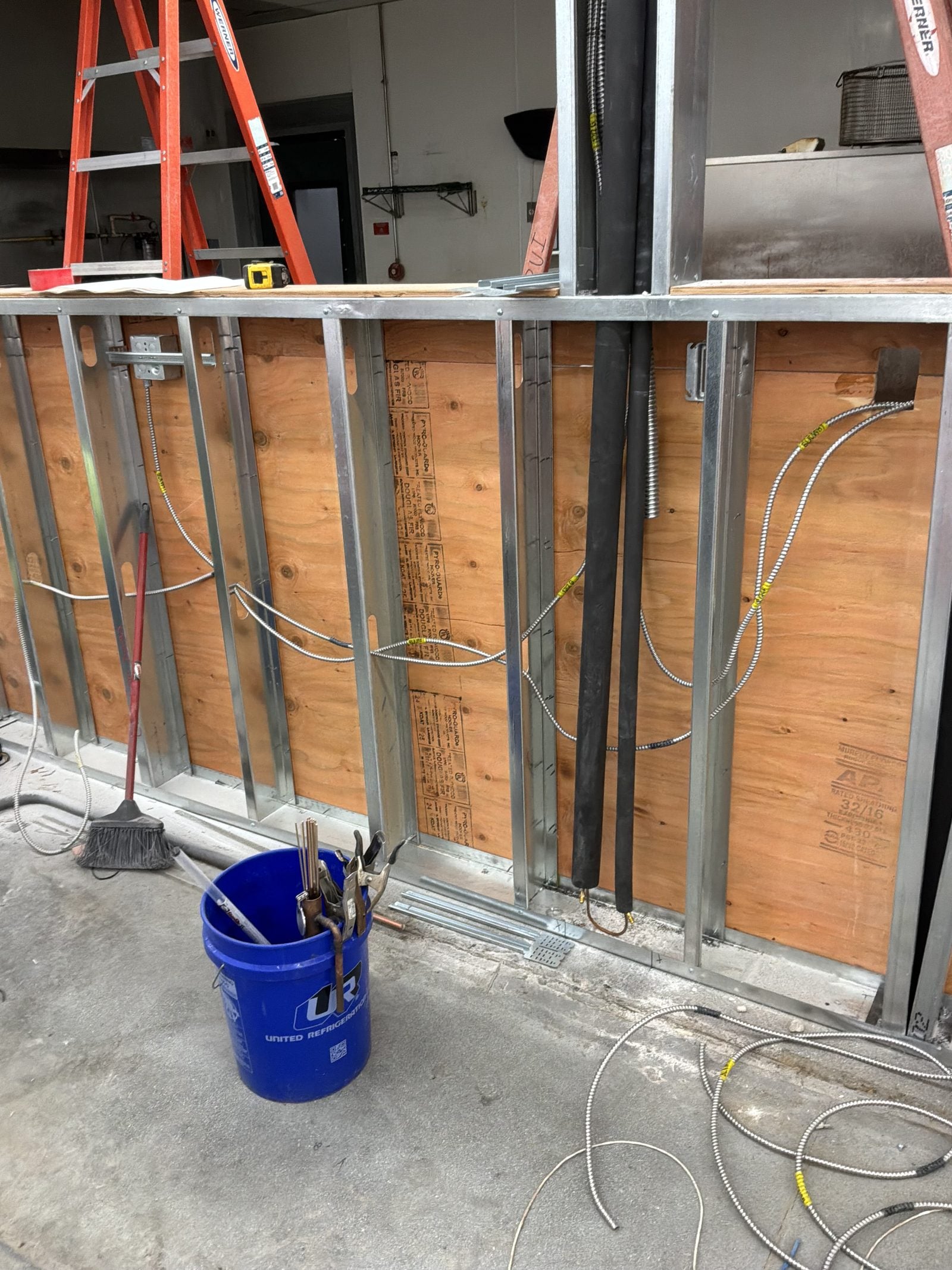 Wall framing with conduit, wiring and outlet boxes, a bucket and a ladder during an overnight remodel at WinCo Foods in Hemet, CA