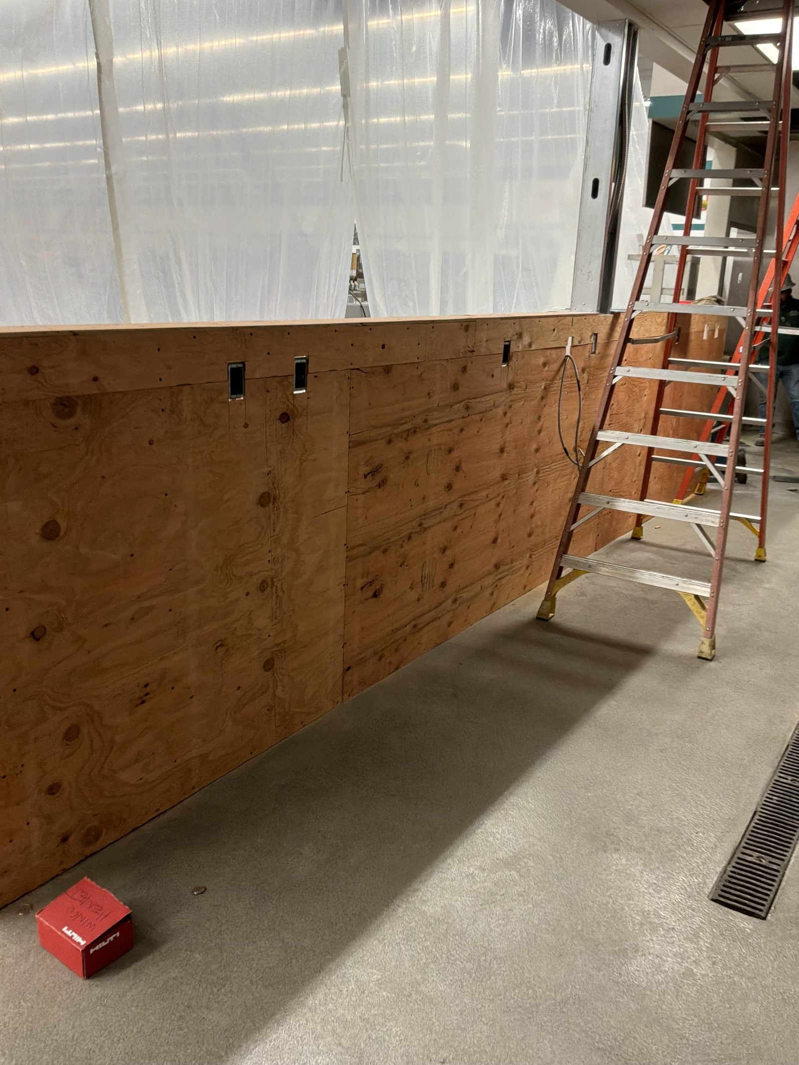 Wood-backed wall with outlet boxes and a coil of flexible conduit on the floor at WinCo Foods in Hemet, CA